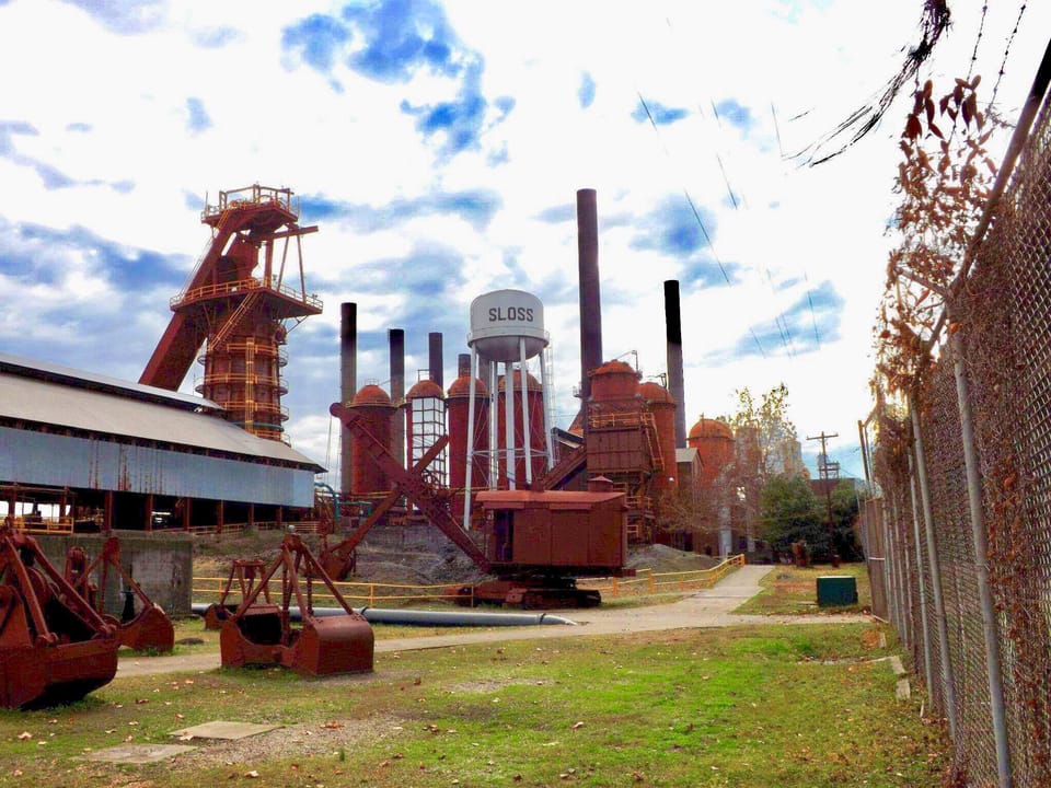 The Sloss Furnaces blast-furnace complex seen from the perimeter walkway along the site fence, with the water tower lettered 'SLOSS' and furnace equipment in the foreground, December 2012.