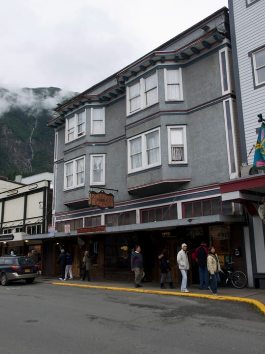 The full three-story Victorian facade of the Alaskan Hotel on South Franklin Street, Juneau, Alaska, with the mountainside behind it.