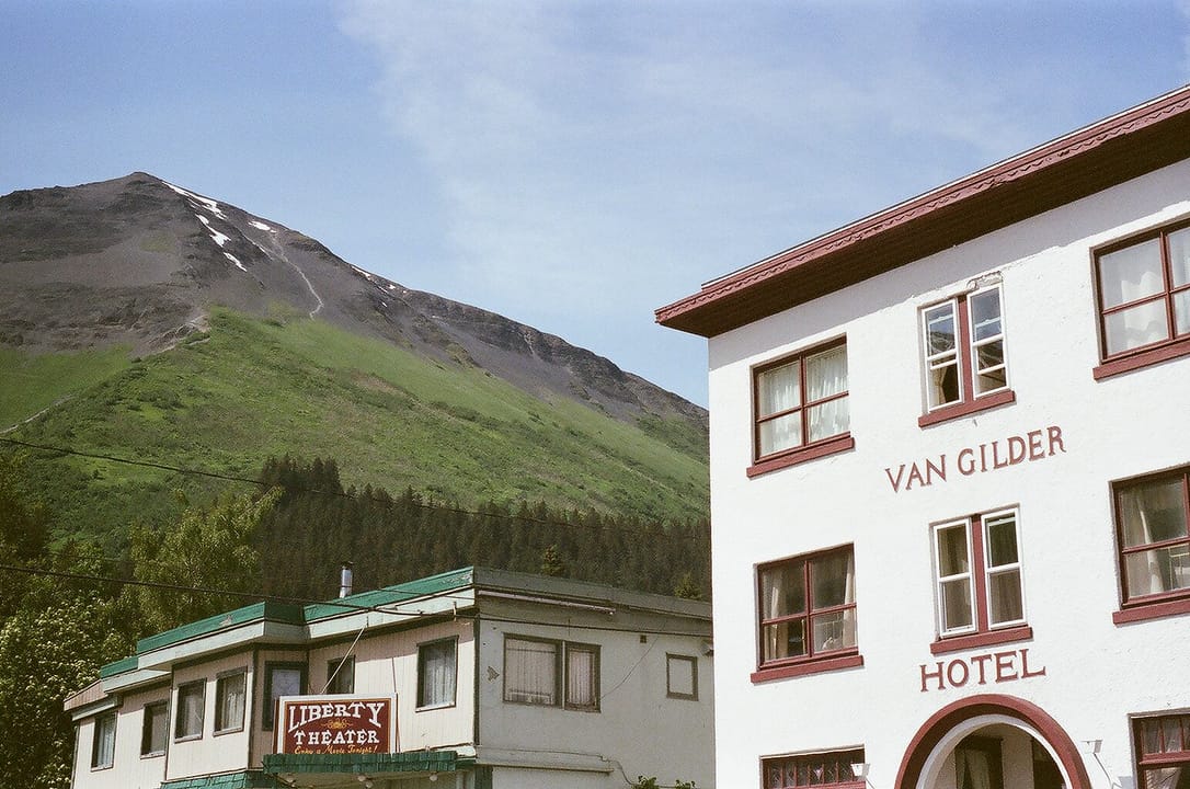 The Van Gilder Hotel and the neighboring Liberty Theater building in Seward, Alaska, in summer, with a green mountainside behind.