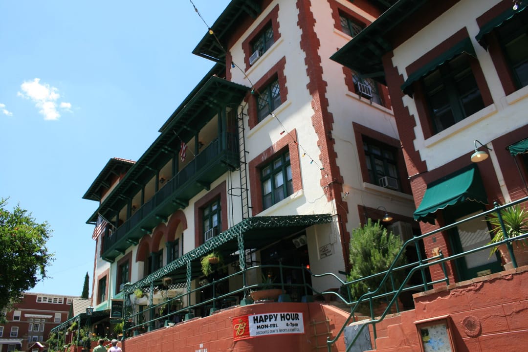 An upward angled street view of the Copper Queen Hotel's green-balconied facade, with its "Happy Hour" sign, Bisbee, Arizona.