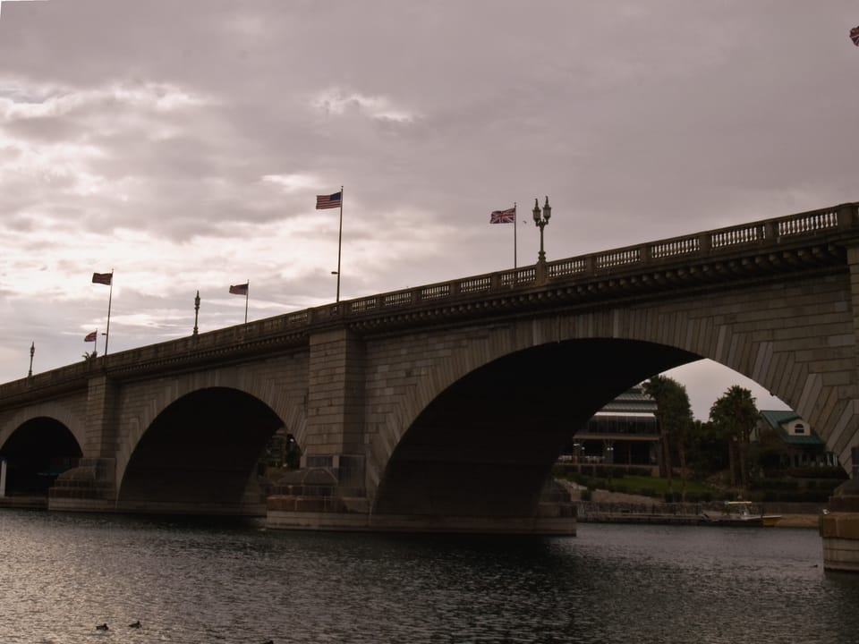 The full bridge span under a moody, overcast sky with flags flying along the balustrade, Lake Havasu City, Arizona.
