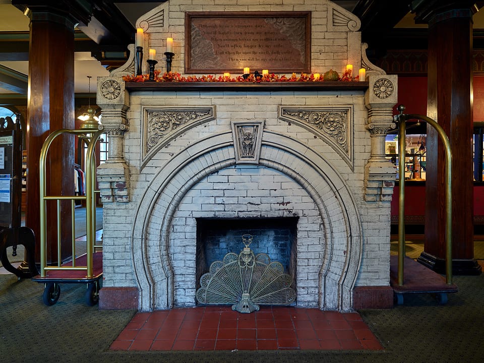 The white-brick lobby fireplace of the Crescent Hotel, with a brass fan screen, bellhop cart and red tile hearth, Eureka Springs, Arkansas, 2020.