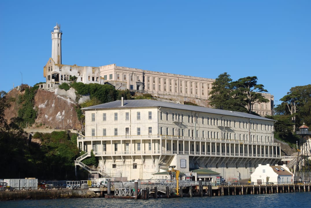 A bright daytime view from the water of Alcatraz's lighthouse, main cellhouse and dock buildings, San Francisco Bay.