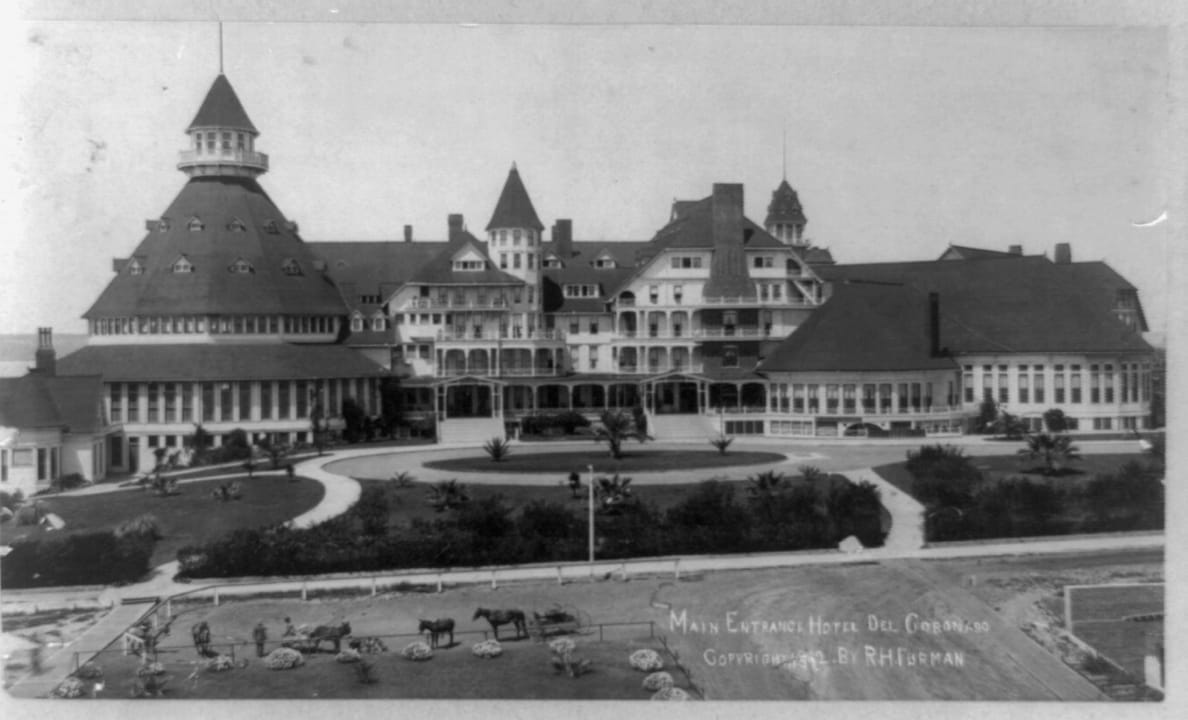 Main entrance of the Hotel del Coronado, Coronado, California, c.1892 -- carriages and horses wait at the circular entrance drive beneath the hotel's conical turret and red-shingled wings. Caption 'MAIN ENTRANCE HOTEL DEL CORONADO, COPYRIGHT 1892 BY 