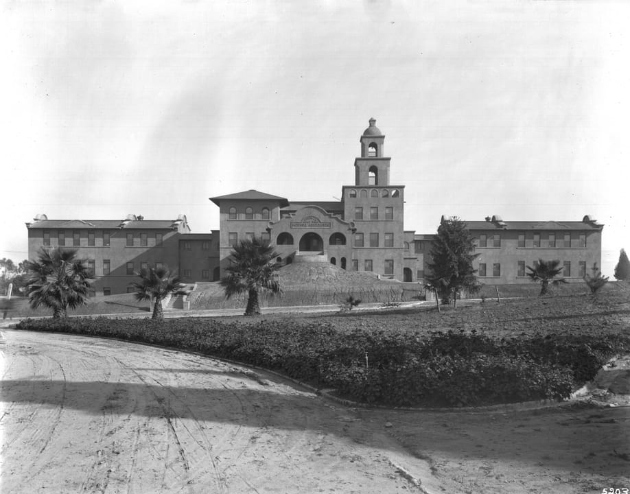 The Santa Fe Railroad Hospital (now Linda Vista Community Hospital) from the dirt road opposite Hollenbeck Park, Boyle Heights, Los Angeles, circa 1905, with a sign reading 'Santa Fe Coast Lines Hospital Association' over the entrance