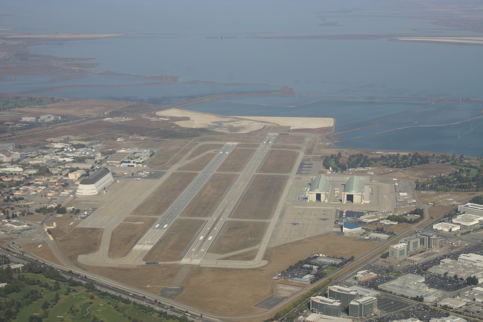 Aerial photograph of Moffett Federal Airfield in Mountain View, California, showing the iconic immense historic naval airship hangars on the runway complex