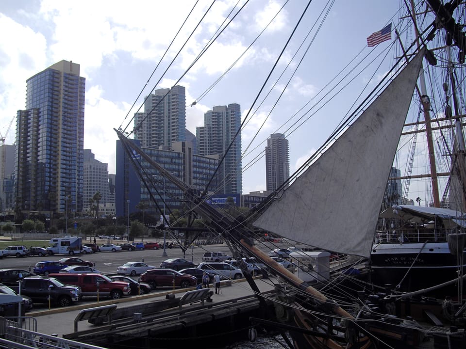 Looking up at the Star of India's rigging and a partially furled sail, with the downtown San Diego skyline behind.