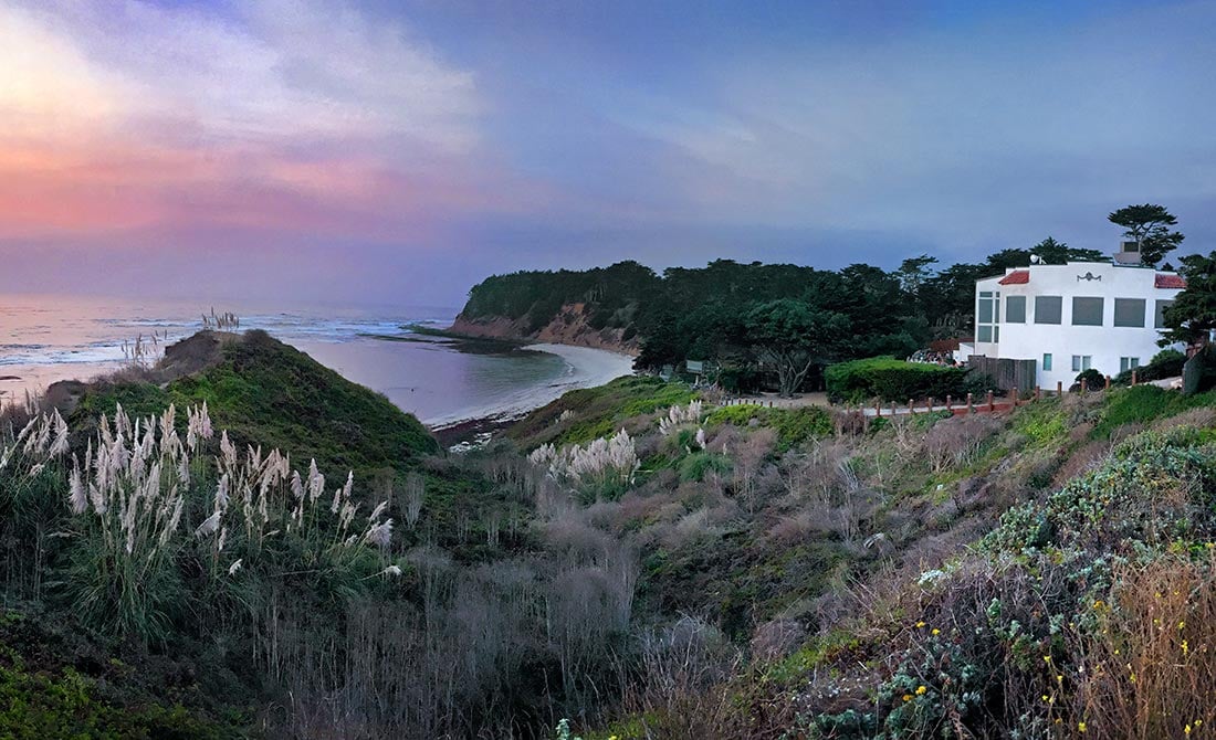 Exterior of Moss Beach Distillery atop the Pacific coastal cliffs at sunset, with pampas grass and ocean below.