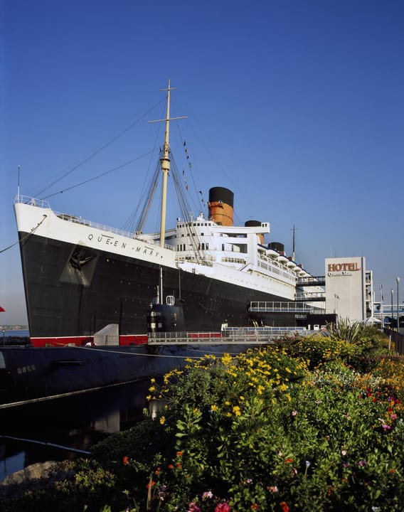 The RMS Queen Mary ocean liner permanently moored at Long Beach, California, its three red funnels and black hull visible from the harbor