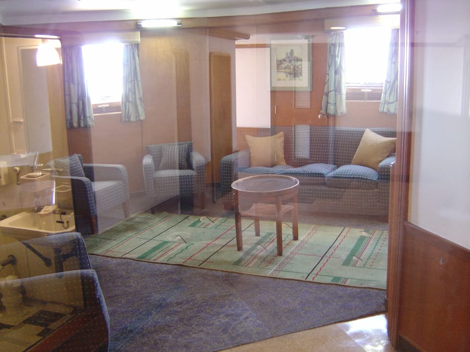 The sitting area of the Captain's Cabin suite aboard the Queen Mary, with a built-in sofa, portholes and period furnishings.