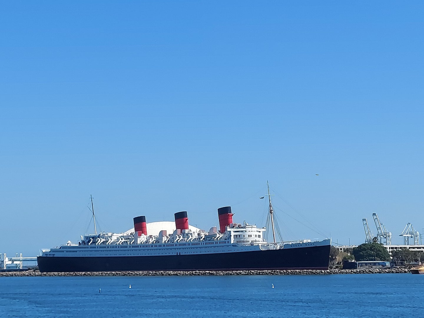 The RMS Queen Mary ocean liner permanently moored at Long Beach, California, its three red funnels and black hull visible from the harbor