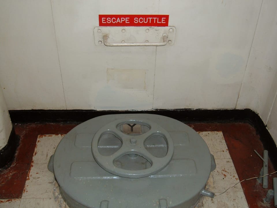 A labeled deck escape scuttle hatch aboard USS Hornet (CV-12), a distinctive shipboard detail visitors see on the museum tour.
