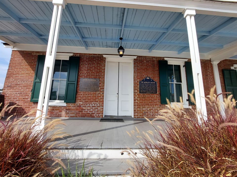 Close view of the Whaley House's front porch, brick facade, green shutters and entrance door under the covered colonnade.