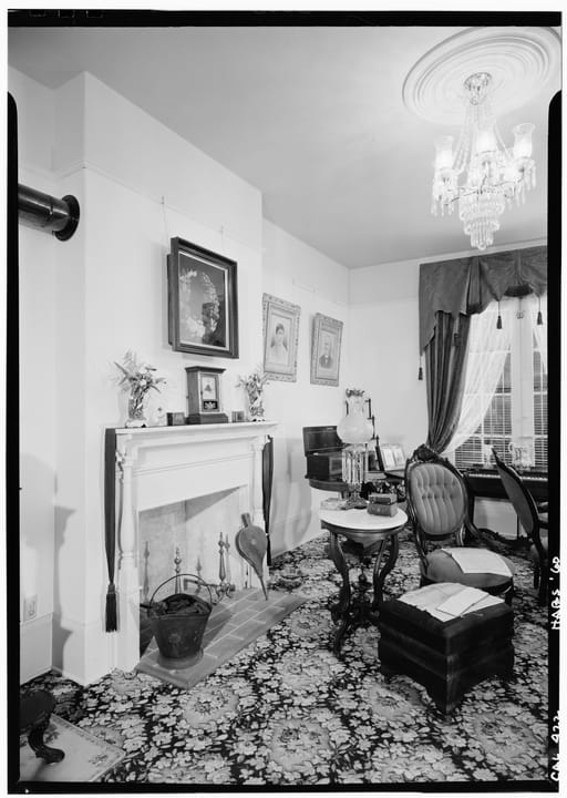 The furnished Victorian-era living room of the Whaley House, with fireplace, chandelier and period portraits, photographed for the Historic American Buildings Survey in 1960.