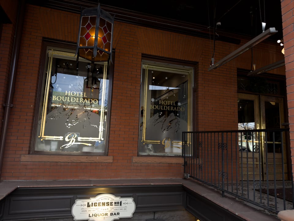 A close evening view of the Hotel Boulderado's ground-floor street windows, lettered "Hotel Boulderado", beside the building's liquor-license plaque.