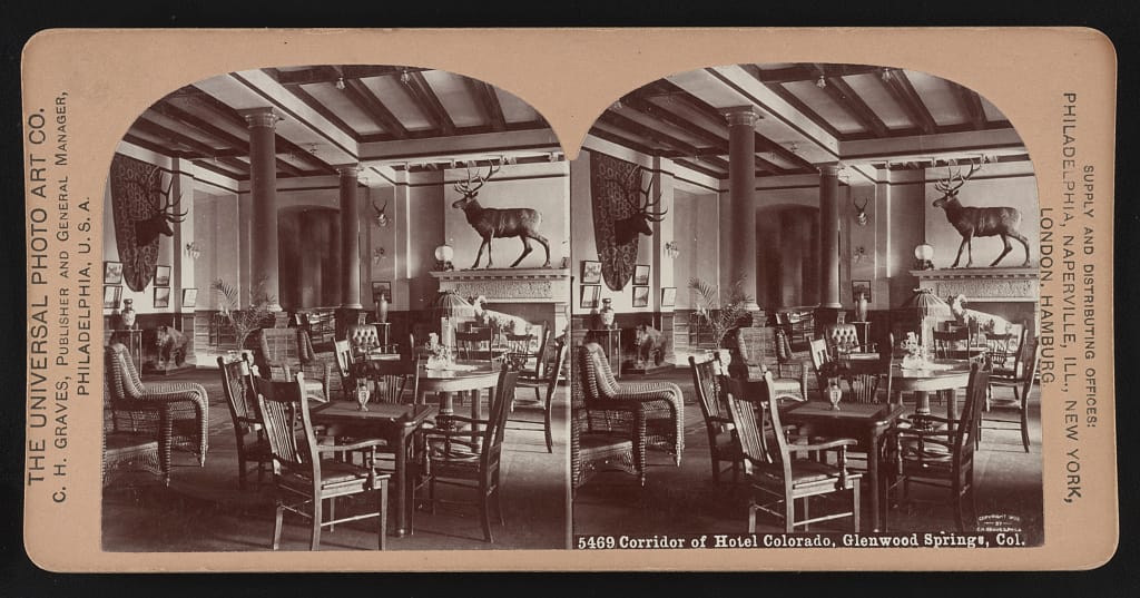 Stereograph of a dining corridor inside the Hotel Colorado, Glenwood Springs, Colorado, circa 1901, with mounted deer heads and set dining tables.