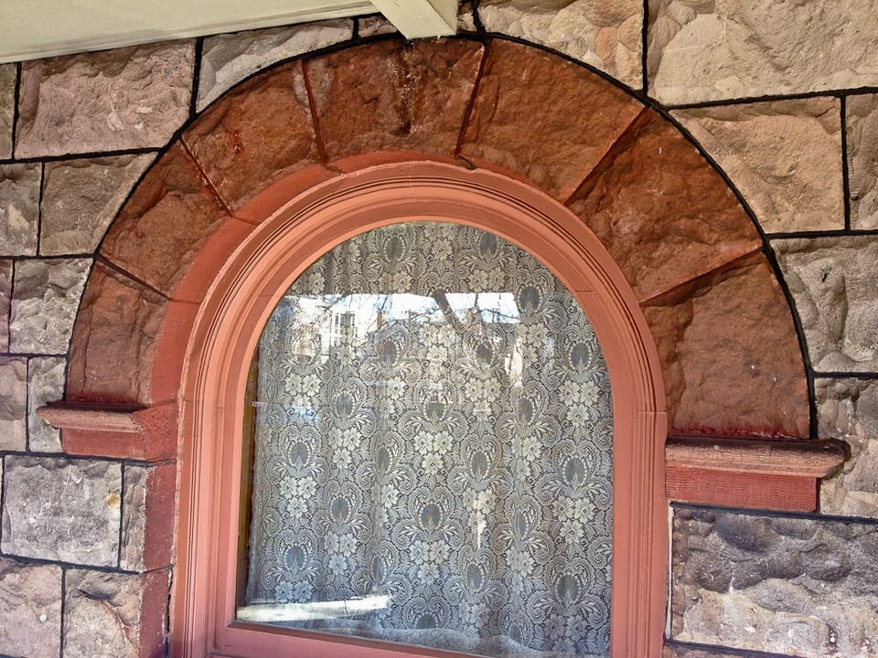 A close detail of a round-arched front window with lace curtain, set in rock-faced stone, on the Molly Brown House, Denver, Colorado.