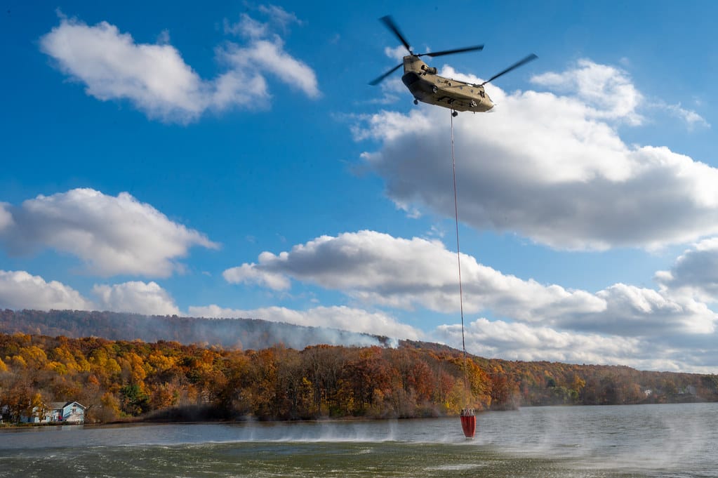 A CH-47 Chinook helicopter belonging to the Connecticut National Guard's 169th Aviation Regiment prepares to gather water from a local lake to dump on a brushfire burning on Lamentation Mountain in Berlin, Connecticut Oct. 23, 2024. This was the first time since 1995 that Connecticut National Guard 