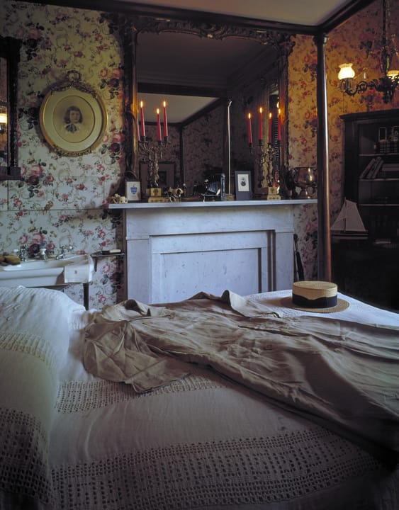 A period bedroom in the Rockwood mansion museum, with floral wallpaper, a canopy bed and a mantel mirror, Wilmington, Delaware.