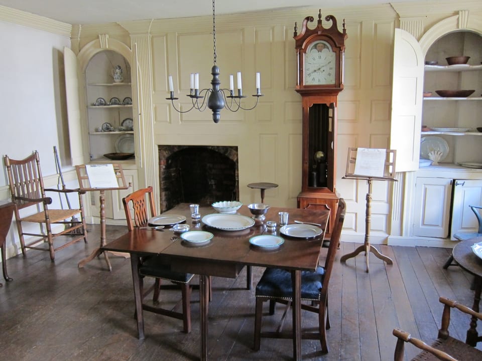 The second-floor dining room of the Old Stone House, set with period furniture, a tall-case clock, corner cupboards and a fireplace.