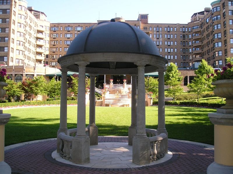 The stone gazebo on the lawn of the Omni Shoreham Hotel in Washington, D.C., with the hotel's tan-brick wings and rounded balconied bays rising behind it.