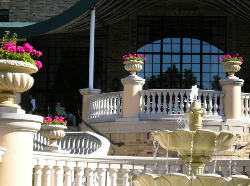 A tiered fountain and balustrade on the garden terrace of the Omni Shoreham Hotel, with the hotel's large arched window and green canopy behind.