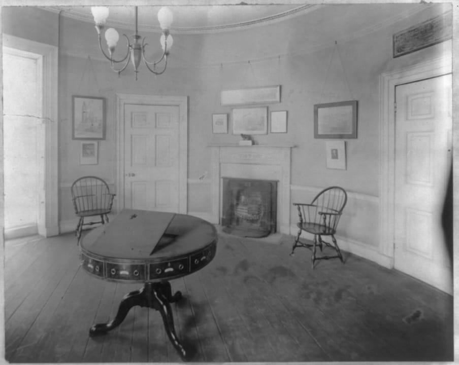 A furnished room inside the Octagon House, with a round center table, Windsor chairs and a fireplace, photographed in 1913.