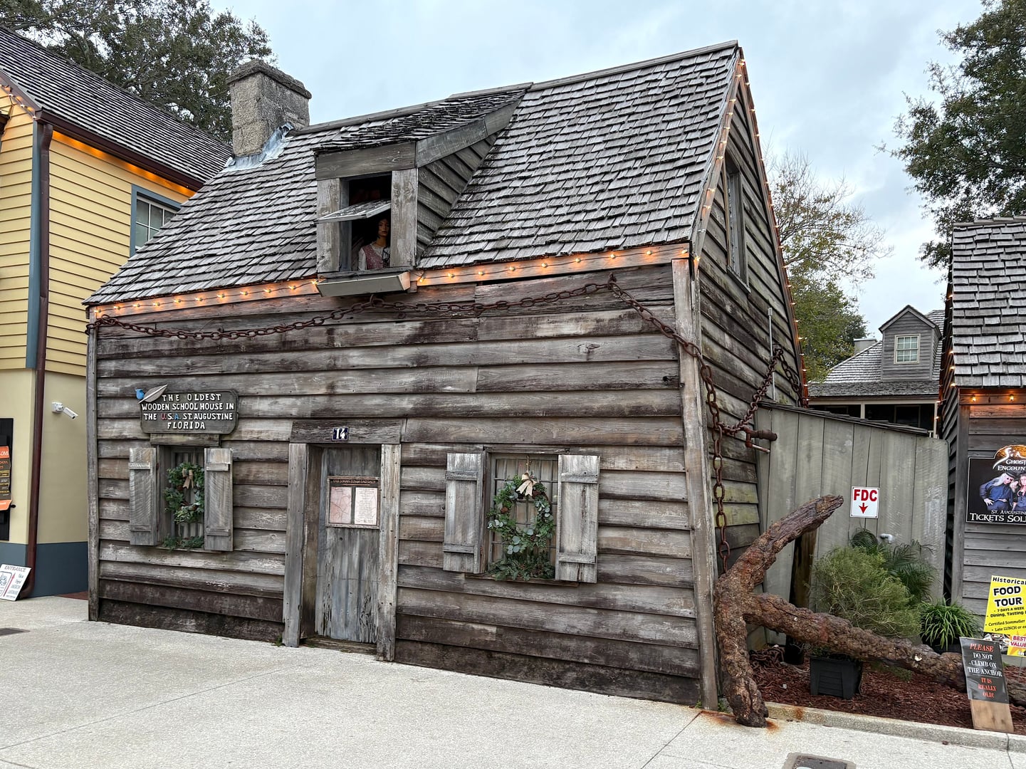 Exterior of the Oldest Wooden Schoolhouse at 14 St. George Street, St. Augustine, Florida — a circa-1716 bald-cypress-and-cedar colonial building wrapped in a large iron chain