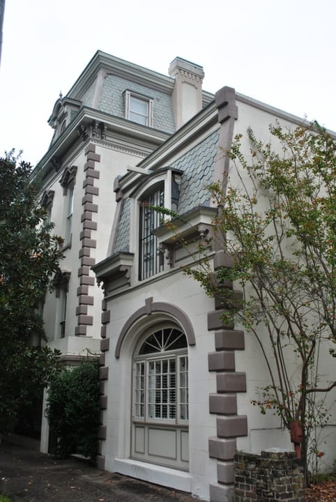 The north side of the Hamilton-Turner Inn in Savannah, where a stuccoed wing with an arched, shuttered window stands below the house's mansard roof and quoined corners.