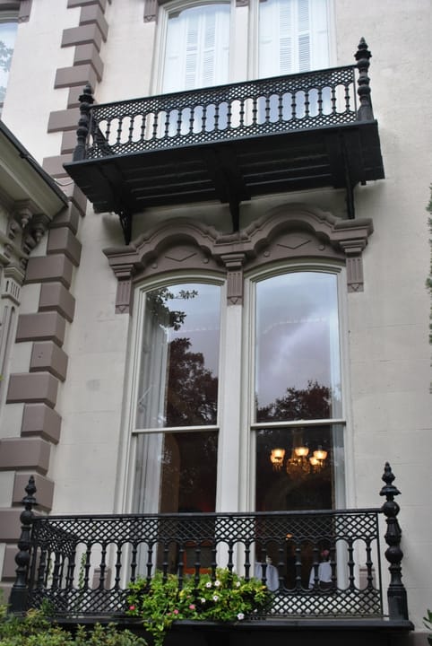 A tall double window with a moulded hood and a cast-iron balcony on the front of the Hamilton-Turner Inn in Savannah, with the darker quoins at the corner.