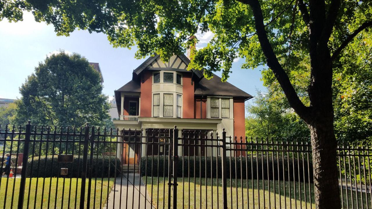 The Tudor Revival-style Margaret Mitchell House glimpsed through its iron perimeter fence and shade trees, Atlanta, 2019.