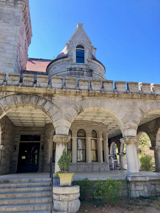 Detail of Rhodes Hall's arched granite porch with its crenellated parapet, stone columns and conical-roofed turret, Atlanta, March 2019.