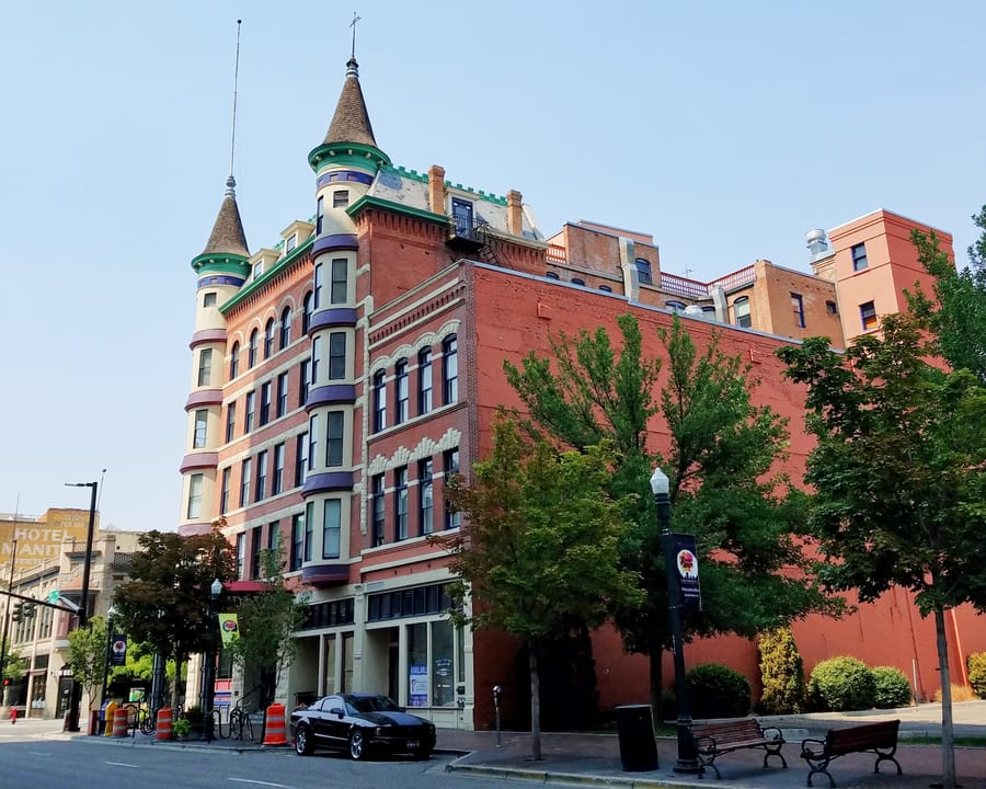 The Idanha Hotel at Tenth and Main in downtown Boise, seen from the street with its twin conical-roofed corner turrets, banded red brick and a long brick side wall, daytime, August 2018.