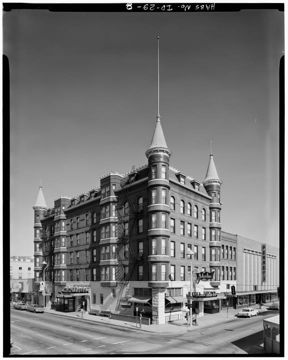Historic American Buildings Survey photograph of the Idanha Hotel from across the intersection of Main and 10th Streets, Boise, showing all six stories, the corner turrets, flagpole and the hotel's mid-century signs; undated survey documentation, evi