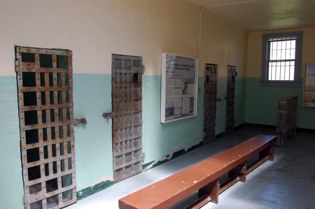 Interior of the Women's Ward at the Old Idaho State Penitentiary, Boise, Idaho, with original cell doors preserved along the wall and a museum display panel.
