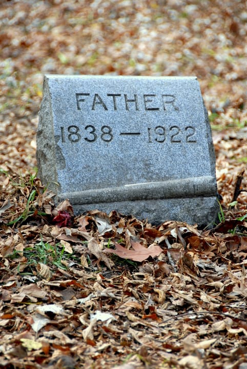 A dirt path winding past scattered headstones at Bachelor's Grove Cemetery, autumn foliage overhead.