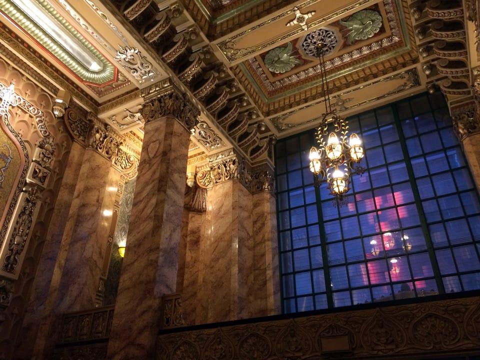 Interior view of the lobby's painted ceiling, chandelier and a stained-glass window, same photo session as the other lobby images.
