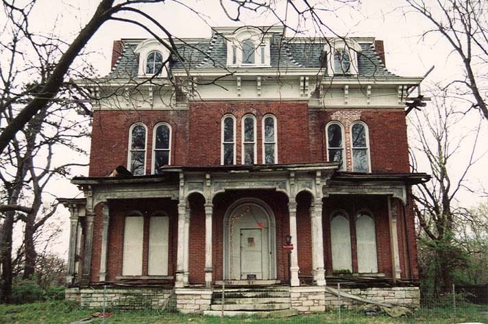 The front of the McPike Mansion in April 2005, seen across the lawn, with the ground-floor openings boarded and the porch weathered, Alton, Illinois.