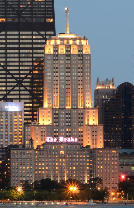The Drake Hotel lit up at night, its rooftop 'The Drake' sign glowing above the Gold Coast skyline, seen from North Avenue Beach.
