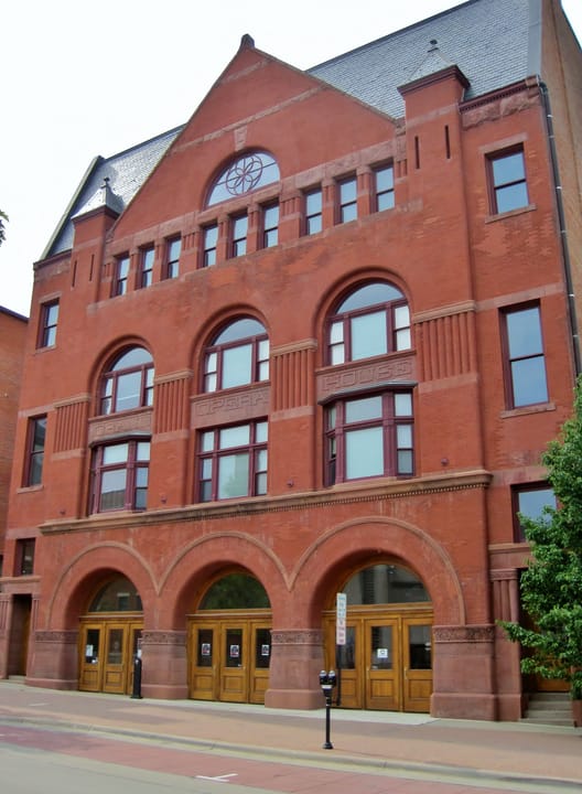 Straight-on street view of the Grand Opera House's arched ground-floor entrances and upper facade, Dubuque.