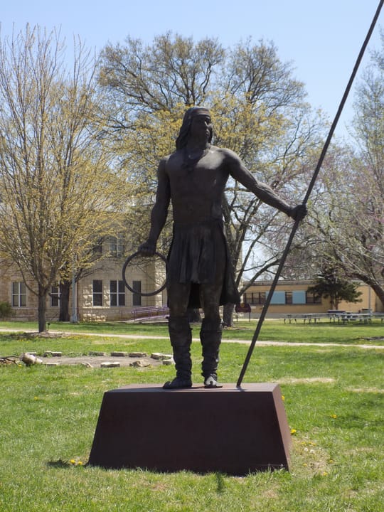 A bronze statue, made by Craig Goseyun, entitled "Apache Loop and Pole Player". Currently on loan by Haskell Indian Nations University.