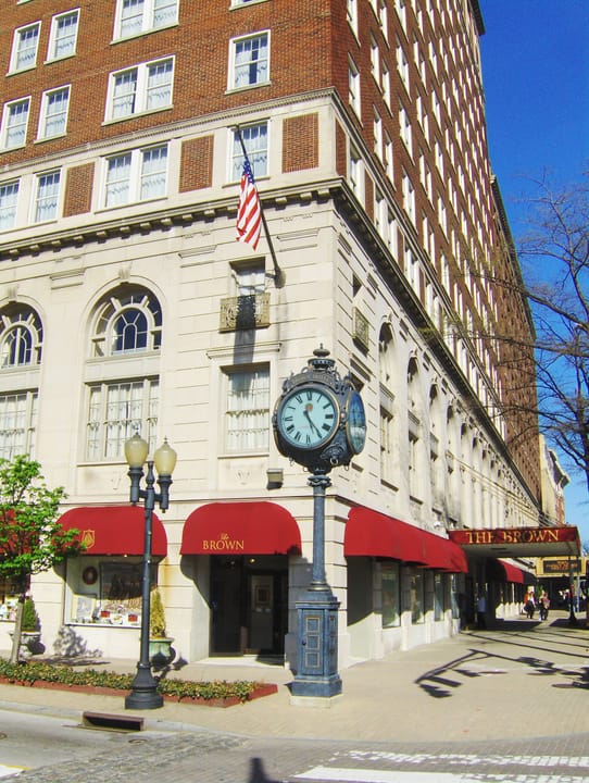 Street-corner view of the hotel's lower stories with the sidewalk clock, flag and red 'THE BROWN' awnings, a different angle and year from the other exterior images.
