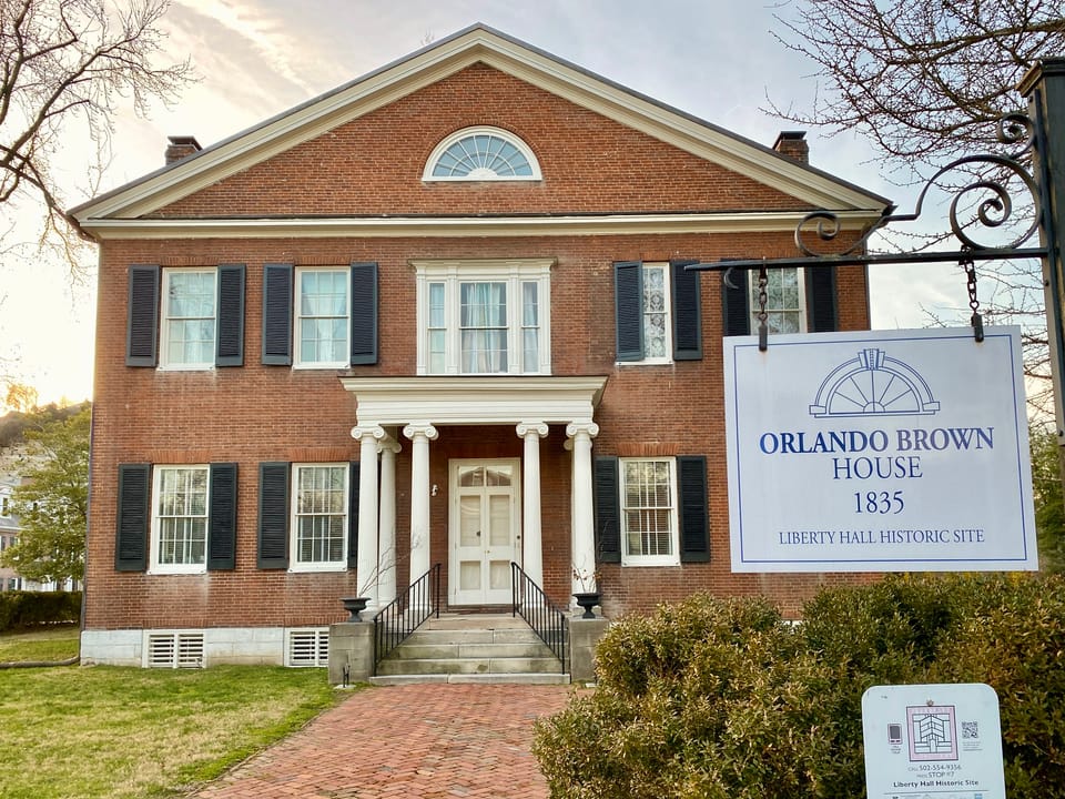 The Orlando Brown House at dusk, the 1835 Greek Revival companion building on the Liberty Hall Historic Site grounds built for Senator John Brown's son, with its hanging sign reading 'Orlando Brown House 1835, Liberty Hall Historic Site'.