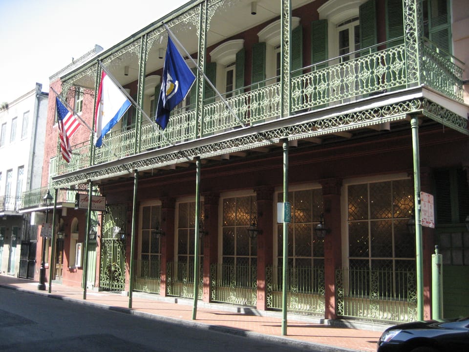 Corner view of Arnaud's ornate cast-iron balconies on Bienville Street, flying the US, Louisiana and French Quarter flags.