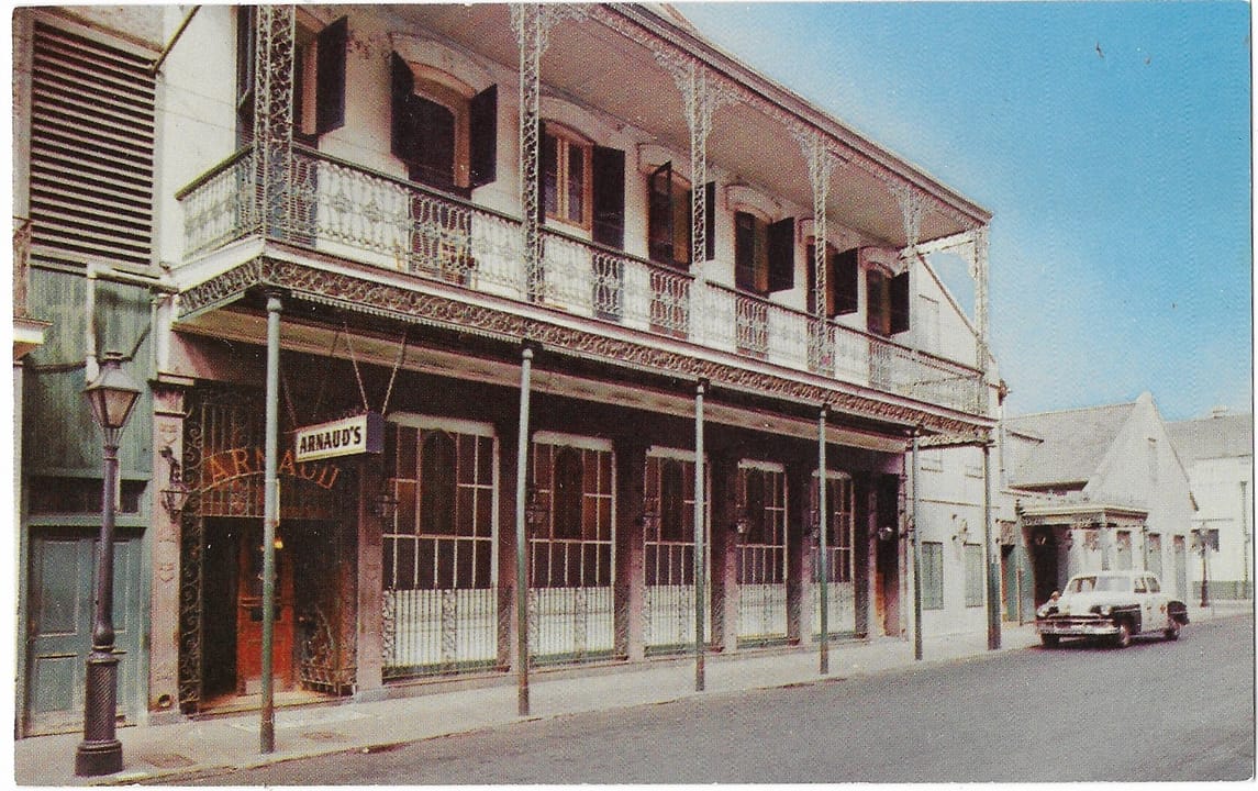 Mid-20th-century postcard view of Arnaud's Restaurant on Bienville Street, with a period taxi parked outside.