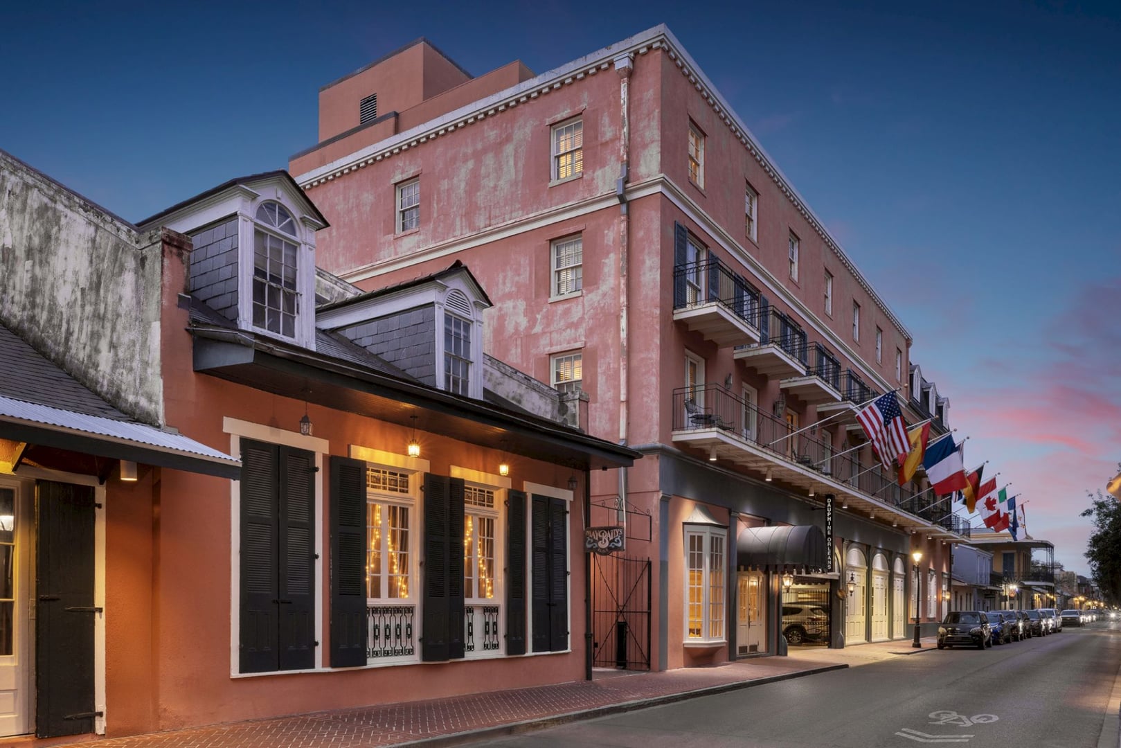 Historic pink Creole-style facade with wrought-iron balconies at the Dauphine Orleans Hotel in the New Orleans French Quarter, lit at dusk.