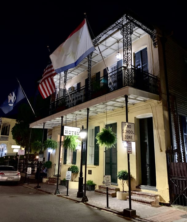 The Andrew Jackson Hotel at 919 Royal Street in the French Quarter, New Orleans, at night, with its lit iron-lace balcony, flags and hanging ferns, September 2022.