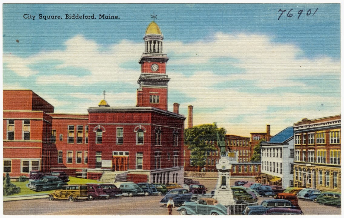 Linen postcard of Biddeford City Hall, the brick building and clock tower that house City Theater, seen across City Square with the soldiers' monument and parked cars, about 1930-45.