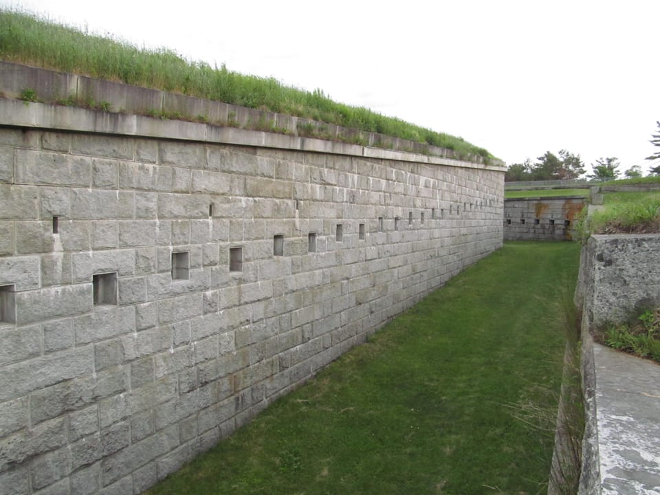 Long granite rampart wall with gun embrasures and turf-covered top, Fort Knox, Prospect, Maine.