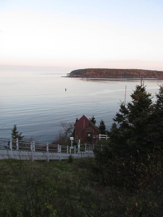 The light station's wooden stairway down to the fog-signal house on the shore at Owls Head Light, with Penobscot Bay and a distant island beyond.